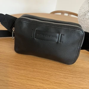 Väska  - Snygg svart väska från Calvin Klein Jeans. Knappt använd, nypris 899kr. Mått H14cm, L21cm & B7cm.