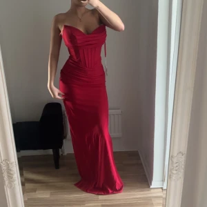 Röd balklänning - Säljer en elegant röd axelbandslös långklänning med en tight passform. Klänningen har en vacker drapering och en smickrande siluett. Perfekt för speciella tillfällen.