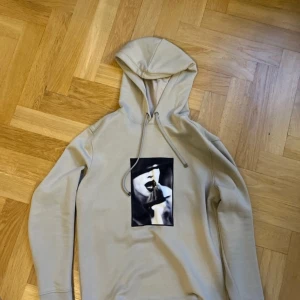 Limitato hoodie - Säljer en beige hoodie med ett unikt tryck på framsidan från Ellen Von Unwerth. Hoodien har en klassisk design med dragsko i huvan och långa ärmar. Perfekt för en stilren och bekväm look.