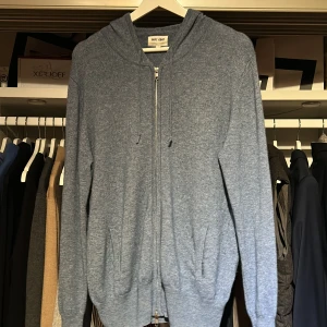 Blå hoodie från Soft Goat  - Säljer en stilren blå hoodie från Soft Goat. Den har dragkedja framtill och justerbar huva med snören. Perfekt för en avslappnad look.