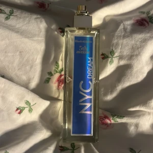 Elizabeth Arden 5th Avenue NYC Parfym - En nästan oanvänd parfym från Elisabeth Arden.  Huvudanteckningar: Rosa peppar, Bourgogne vinbär knoppar absolut Hjärtanteckningar: Marocko apelsinblomma absolut, ros, tuberos, jasmin absolut från Egypten Bakgrundsanmärkningar: Virginia cederträ, Nya Kaledoniens sandelträ, Ambertonic Juiceens färg kan variera beroende på ingredienserna av naturligt ursprung Sinnestillstånd: Förtrollande, glad, utan gräns. (Själv så tycker jag den doftar elegant med lite vanilj) Ord pris; 200kr