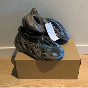 Yeezy Foamrunners - Säljer ett par Adidas Yeezy Foam Runner MX Carbon med unik marmorerad design i svart, blått och grått. Skorna har en futuristisk form med många hål för ventilation. Perfekt för dig som gillar att ha det luftigt runt foten. Kvitto finns och bara att höra av sig vid funderingar😀