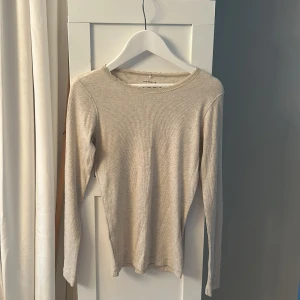 Beige ribbad långärmad tröja från Name It - Säljer en beige ribbad långärmad tröja från Name It. Tröjan har en söt spetsdetalj runt halsringningen och är tillverkad i mjukt material. Tröjan är strl 134/140 men passande som 146/152
