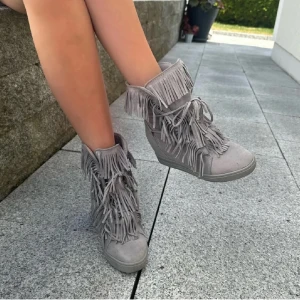 Grå boots med fransar - Säljer ett par grå boots med högt skaft och massor av fransar. Skorna har snörning framtill och är tillverkade i mocka. Perfekta för mig som har storlek 38-39. Tryck på KÖP NU så postar jag så snabbt som möjligt. (Lånade bilder så kom privat för egna bilder) 