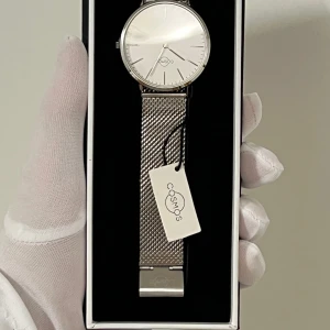 Äkta safir glas Först till kvarn - Oanvänd original Cosmos Sweden Klocka – Mercury i rostfritt stål - Helt ny och oanvänd armbandsklocka från det svenska märket Cosmos. Modellen Mercury har en stilren vit urtavla och ett silvrigt mesharmband i rostfritt stål. Designen är tidlös och passar både formella och avslappnade tillfällen.  Nyckelfunktioner • Urverk: Japanskt kvartsurverk • Glas: Safirglas • Boett: Rostfritt stål (316L) • Tjocklek på boett: 7 mm • Diameter: 40 mm • Armband: Mesharmband i rostfritt stål med snabbfäste (20 mm bredd) • Vattentålighet: 3 ATM • Vikt: ca 85 g • Stil: Tidlös, kö