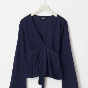 Mörkblå omlottopp med knyt - Säljer en mörkblå omlottopp med v-ringning och långa ärmar. Toppen har knyt i midjan som ger en fin passform och lätt struktur i tyget. Perfekt att styla med jeans eller kjol.