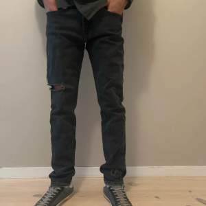 Säljer ett par svarta Levis 502 jeans med klassisk femficksdesign och en liten slitning på vänster knä. Jeansen har rak passform och är tillverkade i denim. 