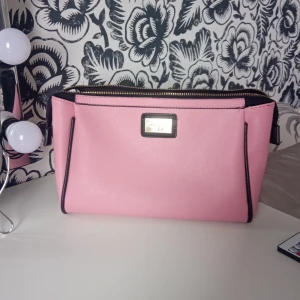 Rosa handväska med svarta detaljer - Säljer en söt rosa handväska med svarta kanter och guldfärgad dragkedja. Väskan har en innerficka med dragkedja och är perfekt för att bära dina viktigaste saker. Enkel och stilren design som passar till många tillfällen. Jag sälger denna för jag har en annan 