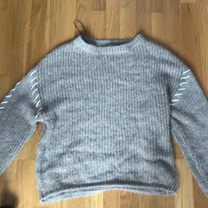 Stickad beige tröja från Amisu - Mysig stickad tröja i ljusgrått från Amisu. Tröjan har lång ärm och coola snörningsdetaljer längs ärmarna. Perfekt för kyliga dagar och enkel att matcha med jeans eller kjol.