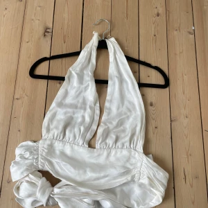 Vit  halterneck topp - Säljer en vit topp med halterneck och breda knytband i midjan. Toppen är ärmlös och har en djup v-ringning framtill. 