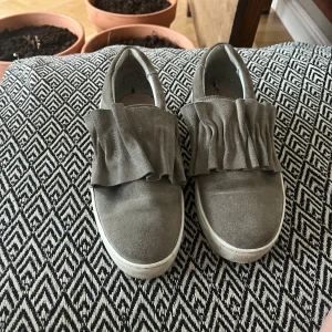 Grå mockasneakers med volangdetalj - Säljer mina jätte fina gråa sneakers i mocka med volangdetaljer. Jag använde dem ett få tal gånger förra sommaren men har nu vuxit ur dem💞💞