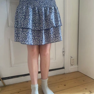 Blå blommig kjol från SHEIN - Supersöt blå kjol med vitt blommönster från shein Rose. Kjolen har två volanger och resår i midjan för extra komfort. Perfekt för dig som gillar en feminin stil. Storlek M men är väldigt stretchig så passar xs-s-m