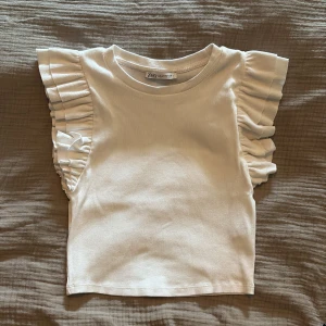 Vit ribbad topp med volangärmar från Zara - Supersöt vit ribbad topp från Zara med volangdetaljer på axlarna. Kort modell