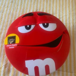 Röd M&M's plåt låda - Cool rund låda i form av den röda M&M's-karaktären. Lådan tillverkad i metall med tryckt motiv och har ett lock som går att ta av. Perfekt som accessoar eller förvaring av småsaker.