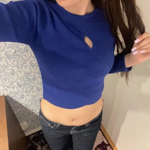 Blå croppad tröja från River Island - Säljer en blå croppad tröja från River Island med lång ärm och en liten cut-out detalj vid halsen. Tröjan är ribbad och sitter tight, perfekt till jeans eller kjol. Superfin färg som sticker ut!