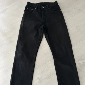 Svarta jeans från Levi's 501 - Klassiska svarta Levi's 501 jeans med raka ben och fem fickor. Byxorna har knappgylf och är tillverkade i bomull. Perfekta för dig som gillar tidlös stil och vill ha ett par jeans som funkar till allt.