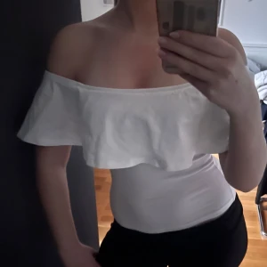 Vit offshoulder topp - Säljer en vit offshoulder topp med volangkant. Toppen är tight och har en snygg, axelbandslös design som passar perfekt till sommaren.
