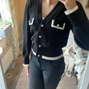 Svart kofta med vita detaljer från Holly & Whyte - Säljer en svart kofta från Holly & Whyte med vita ribbade kanter och dekorativa fickor framtill. Koftan har guldknappar och lång ärm, storlek M, använt ett fåtal gånger, pris kan diskuteras🫶🏻💕💕