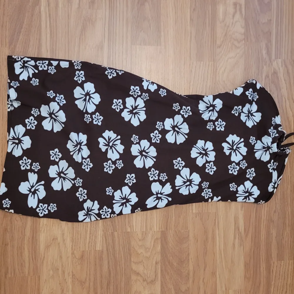 Säljer en brun axelbandslös klänning med blommor. Klänningen har en figurnära passform och är perfekt för sommardagar. Tyget är mjukt och stretchigt för extra komfort.. Mekot.