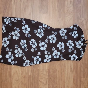 Brun axelbandslös klänning med blommigt mönster - Säljer en brun axelbandslös klänning med blommor. Klänningen har en figurnära passform och är perfekt för sommardagar. Tyget är mjukt och stretchigt för extra komfort.