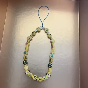 Färgglatt armband med smileys och fruktmotiv - Ett armband med glada smiley- och fruktpärlor i gult, grönt och vitt. Trädd på blå tråd och perfekt som färgglad accessoar. Pärlorna har olika former och motiv, bland annat citron, kiwi och stjärnor.