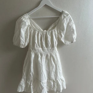 Vit kort klänning med puffärmar och knyt i ryggen - Superfin vit klänning med puffiga kortärmar och v-ringning. Klänningen har knytning i ryggen och dragkedja i midjan ner på sidan av kjolen. Tillverkad i ett lätt linnematerial, perfekt till sommaren💕💕