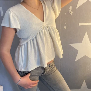 Vit v-ringad blus från Gina Tricot - Säljer en söt vit blus från Gina Tricot i storlek XS. Blusen har v-ringning, korta volangärmar och ett luftigt, rynkat fall. Perfekt till jeans eller kjol och superbekväm tack vare det mjuka materialet.