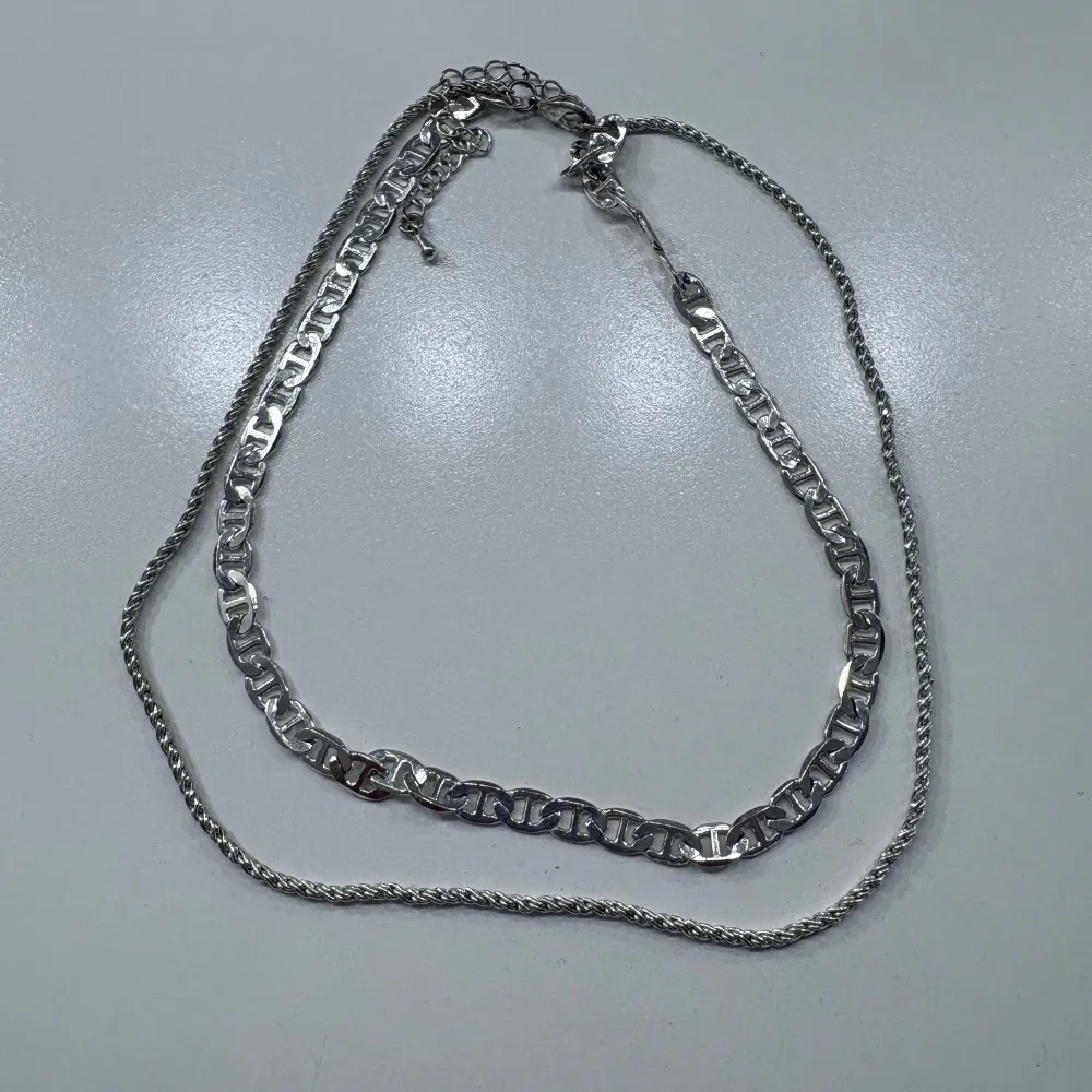 Säljer två snygga halsband i silverfärg. Det ena har en bredare, platt länkdesign medan det andra är tunnare med tvinnad kedja. Perfekta att bära tillsammans eller var för sig för en stilren look.. Asusteet.