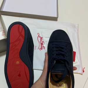 Blåa sneakers från Christian Louboutin - Säljer ett par svarta sneakers från Christian Louboutin i mocka med klassisk röd sula. Skorna har rund tå, platt sula och snörning. Perfekta för dig som gillar stilrena och exklusiva detaljer.