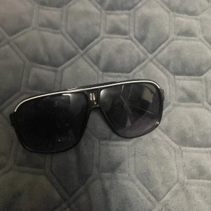 Svarta solglasögon med silvriga detaljer - Snygga svarta solglasögon med bred båge och silvriga detaljer längs ovansidan. Glasen är mörka och ger en cool look, perfekt för soliga dagar. Passar dig som gillar en lite större och markerad stil.