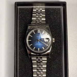 Seiko Datejust 36mm ( Blue Dial ) - Elegant och tidlös Seiko Datejust i 36 mm med en blå urtavla  – en klocka som kombinerar stil med funktion. Utrustad med reptåligt safirglas både fram och bak, vilket ger extra hållbarhet och exklusiv känsla. Klockan är vattentät och har en tydlig datumvisning för extra bekvämlighet. Länken är enkelt justerbar för att passa din handled perfekt.
