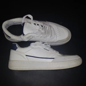Vita sneakers från Björn Borg - Säljer ett par klassiska vita sneakers från Björn Borg med blå detaljer. Skorna har snörning, perforerade sidor och rund tå. Perfekta för en stilren och sportig look. Okej skick 7/10 lite creasade och smutsiga men går att fixa