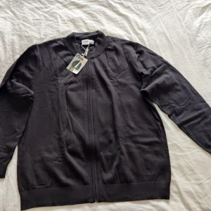 Svart kofta med dragkedja  - Säljer en svart kofta med dragkedja framtill. Tröjan har lång ärm och ribbade muddar vid ärmslut och nederkant. Enkel och stilren design som passar till mycket. Pris 100 