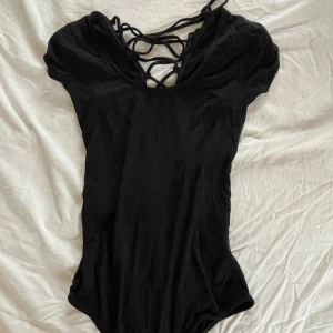 Svart body med snörning - Säljer en svart body med snygg snörning framtill. Djup v-ringning och korta ärmar. Perfekt att styla till jeans eller kjol för en trendig look.
