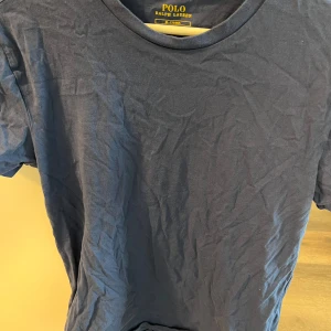 Mörkblå t-shirt från Polo Ralph Lauren - Säljer en klassisk mörkblå t-shirt från Polo Ralph Lauren med rund halsringning och ikonisk broderad logga i vitt på bröstet. Perfekt basic-plagg med enkel och stilren design. Storlek M men passar S