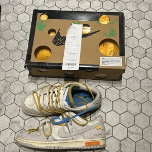 Nike Dunk Low Off-White Lot 34 - Nike Dunk Low Off-White Lot 34 med vit och grå ovandel i skinn och mocka, detaljer i gult och blått samt Off-White-typiska snörningar och taggar. Säljs med originalkartong och kvitto från Kicksnstuff. Priset är inte hugget i sten och är öppen för byten, bara att skriva om du har förslag eller frågor.