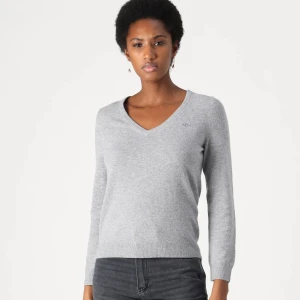 Grå v-ringad stickad tröja från Gant - Säljer en grå stickad tröja från Gant med v-ringning och liten broderad logga på bröstet. Tröjan har lång ärm och är perfekt för lager-på-lager. Superenkel att matcha till olika outfits! Priset går att diskutera.