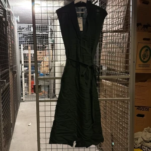 Mörkgrön omlottklänning från Zara - Säljer en mörkgrön omlottklänning från Zara med knytband i midjan. Klänningen är ärmlös och har en djup v-ringning. Perfekt för dig som gillar stilrena och enkla plagg med markerad midja. Den ser svart ut på bild men den är mörkgrön! Ny med lappar kvar 