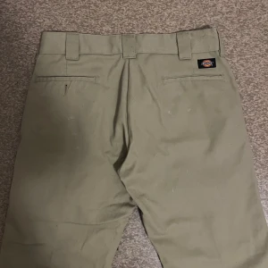 Beiga kostymbyxor, Dickies - Säljer ett par beiga kostymbyxor från Dickies i modellen Slim Straight. Byxorna har hällor för bälte, två bakfickor och klassisk design. 💛