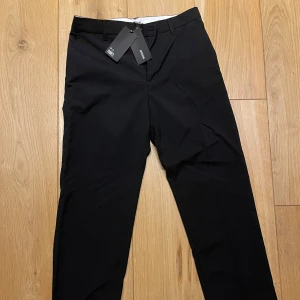 Svarta kostymbyxor från Weekday - Snygga svarta kostymbyxor från weekday med klassisk passform och diskreta fickor. Byxorna har dragkedja och hällor för bälte, perfekta för en stilren look.