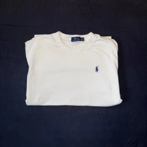 Vit t-shirt från Polo Ralph Lauren - Klassisk vit t-shirt från Polo Ralph Lauren med rund halsringning och liten broderad logga i mörkblått på bröstet. Perfekt basic-plagg med normal passform och korta ärmar. Snygg och enkel att matcha till allt.