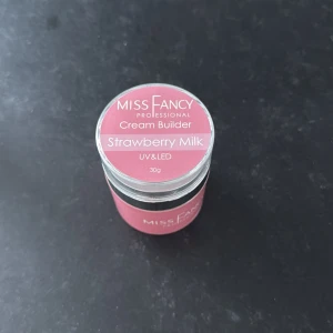 Miss Fancy Cream Builder Strawberry Milk - Miss Fancy Professional Cream Builder i färgen Strawberry Milk. En rosa gelé för nagelförlängning eller förstärkning, anpassad för UV & LED-lampa. Kommer i en rund burk på 30g med skruvlock. Den är ENDAST SWATCHAD. Ordinarie pris är 329 kr