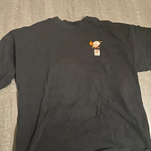 Svart Nike t-shirt med Sole Food-tryck - Säljer en svart t-shirt från Nike med coolt 'Sole Food'-tryck i orange och vitt på ryggen och ett mindre tryck på bröstet. T-shirten har baggy passform och är kortärmad, perfekt för dig som gillar streetwear.