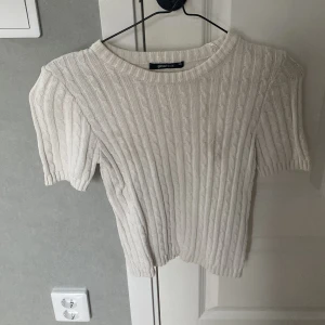 Vit ribbad stickad topp från Gina Tricot - Säljer en vit, kortärmad stickad topp från Gina Tricot i storlek XS. Tröjan har ett ribbat mönster och rund halsringning, perfekt för en stilren och enkel look. Passar bra till både jeans och kjol.