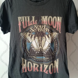 Svart t-shirt med tryck från Gina Tricot - Cool svart t-shirt från Gina Tricot med stort tryck av en fjäril och texten 'Full Moon Horizon Soul Search' på framsidan. Rund halsringning och korta ärmar. Perfekt för dig som gillar statement-plagg och snygga tryck. Väldigt snygg men framförallt bekväm och skön. 15 kr!!! 