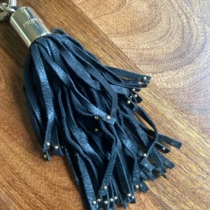 Svart tofs-väska från Juicy Couture ! - Cool svart tofs-väska från Juicy Couture! med fransar i skinn och guldiga metalldetaljer. Perfekt som accessoar till din väska eller nyckelknippa för en extra touch av stil.