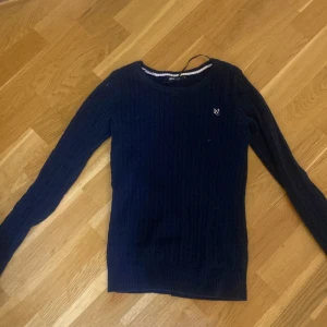 Mörkblå ribbad stickad tröja  - Hej!! Min kompis säljer en mörkblå stickad tröja med diskret logga på bröstet. Tröjan har rund halsringning, ribbad struktur och långa ärmar. Perfekt för lager-på-lager och enkel att matcha med jeans eller kjol.