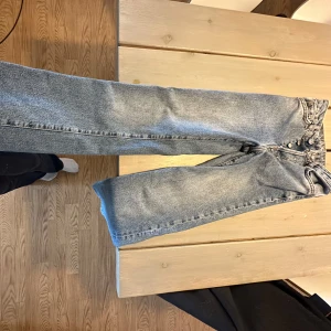 Blå raka jeansbyxor - Säljer ett par klassiska blå jeansbyxor med raka ben och hög midja. Jeansen knappar i gylfen och tydliga sömmar. Perfekta för en avslappnad och tidlös stil.
