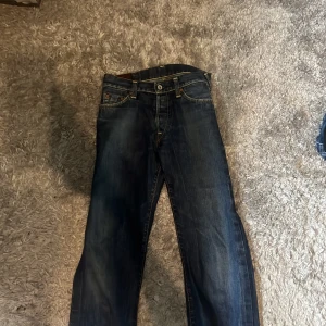 Mörkblå jeans från Evisu - Säljer ett par klassiska mörkblå jeans från Evisu med ikoniska målade detaljer på bakfickorna och patch med logga. 