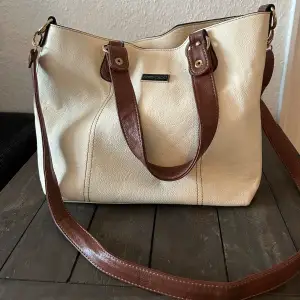 Säljer en snygg beige axelväska från Jimmy choo med bruna detaljer. Väskan har en praktisk dragkedja på baksidan och en rymlig insida med flera fack. Perfekt för både vardag och lite finare tillfällen!